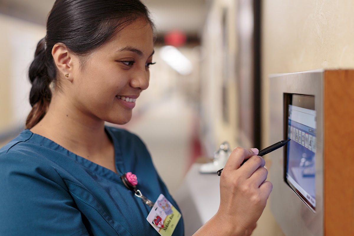 A caregiver at a nurse's computer on the wall in the hallway of Villa Las Palmas